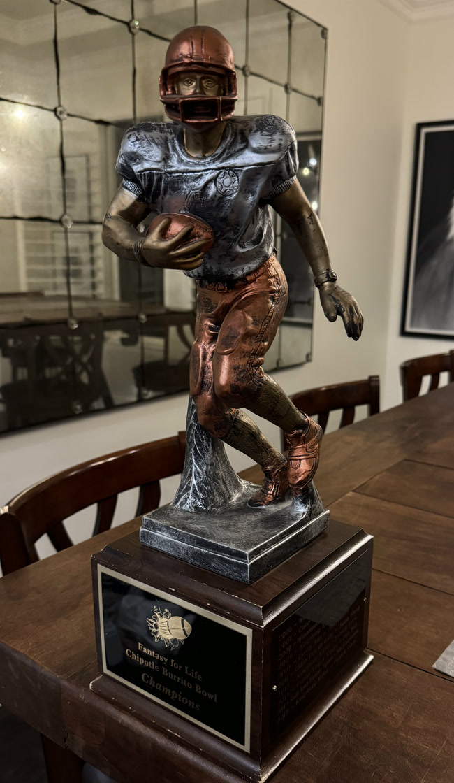The retired championship trophy: a bronze running back on a wooden base, plated Fantasy for Life Chipotle Burrito Bowl Champions