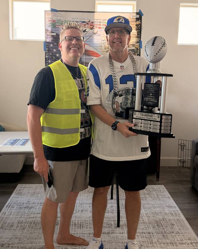 The 2025 champion holding the trophy beside the Toilet Bowl winner in his safety vest
